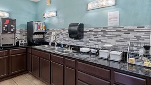 A kitchen with a coffee machine, a hand dryer, and a paper towel dispenser.
