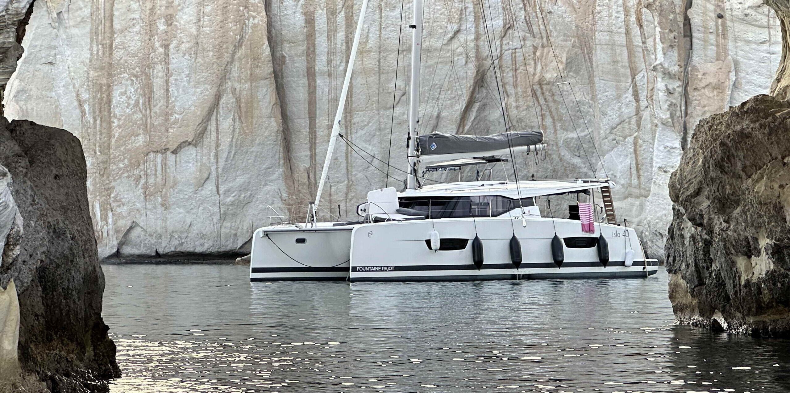 Eine weiße Yacht namens 'FONTAINE PAJOT' liegt an einer steilen Klippe festgemacht.