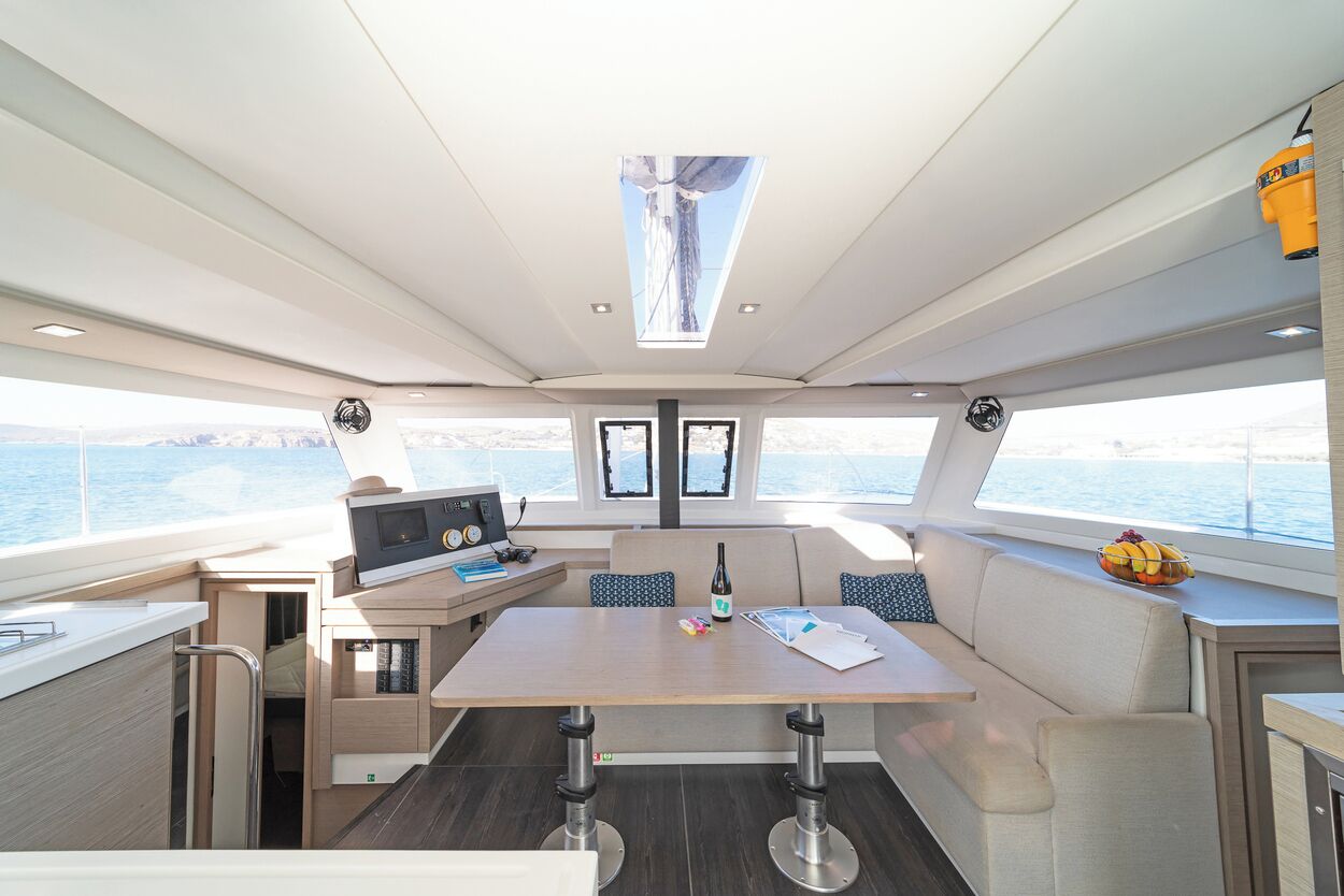 A yacht interior with a dining area, a control station, and a view of the sea.