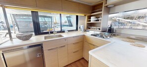 A modern kitchen with a large window, stainless steel appliances, and wooden cabinetry. - Sun-Kissed Sailing Adventure in Islas Sarónicas (Alimos)