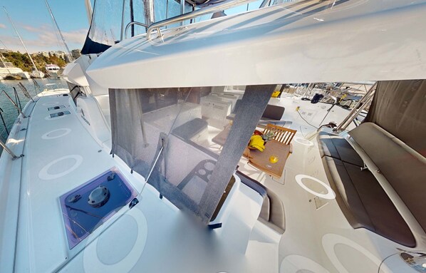 A yacht's deck with a covered seating area, a small table with a banana, and a circular window. - Sun-Kissed Sailing Adventure in Islas Sarónicas (Alimos)