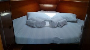 Una cama individual con sábanas blancas y dos toallas enrolladas.