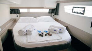 Un lit bien fait, avec des serviettes pliées et des articles de toilette à portée de main, une fenêtre avec des rideaux et une tête de lit agrémentée d’une lampe.