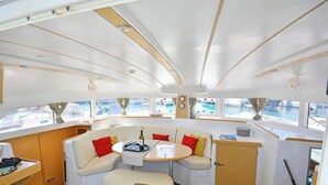 Jachten-Interieur mit Essbereich, einem kleinen Tisch mit einer Flasche und Meerblick durch Fenster.