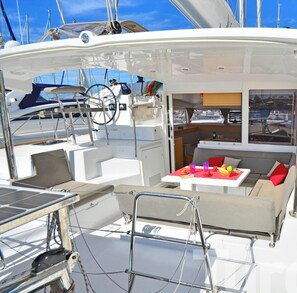 Das Deck einer Yacht mit Essbereich, Steuerpult und Blick auf andere Boote.