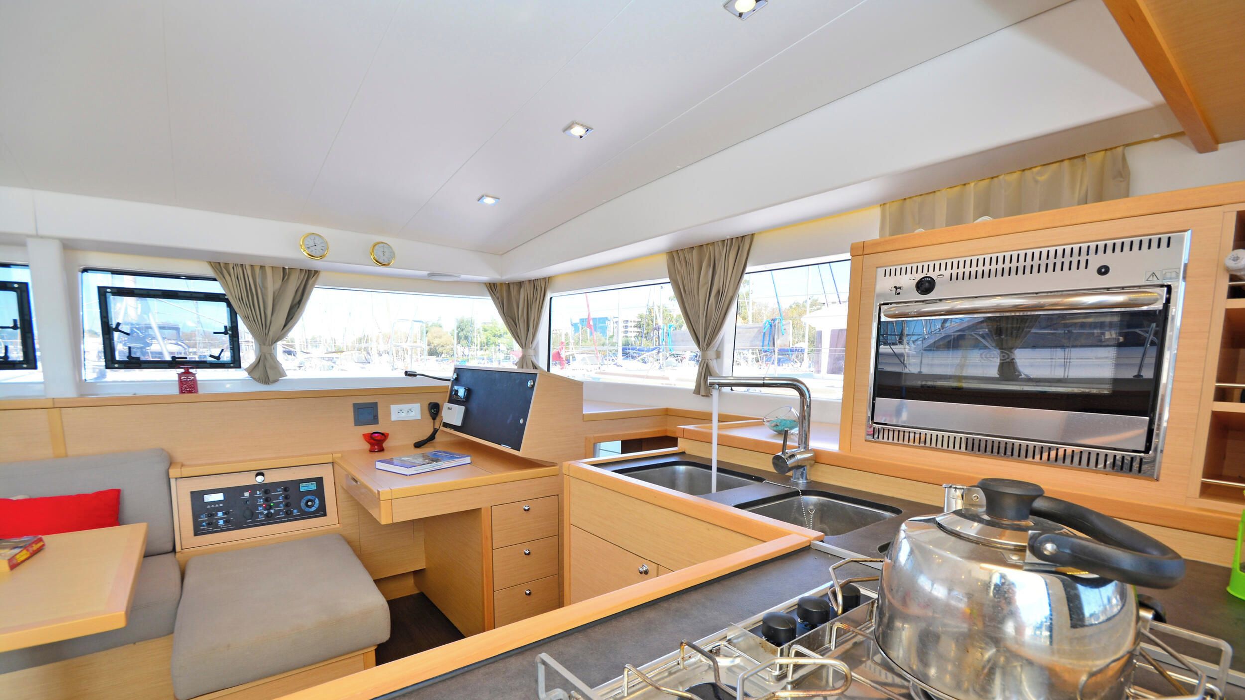 A compact kitchen with a stove, sink, and oven, a control panel, and a window with curtains.