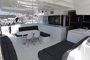 Interior de un barco con comedor, pequeña cocina y zona de estar.
