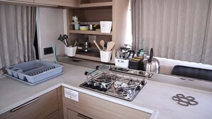Una kitchenette compacta con estufa a gas, repisas para almacenamiento y un ventanal con cortinas.