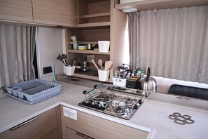 A compact kitchenette with a gas stove, storage shelves, and a window with curtains. - Sun-Kissed Sailing Adventure in Islas Sarónicas (Alimos)