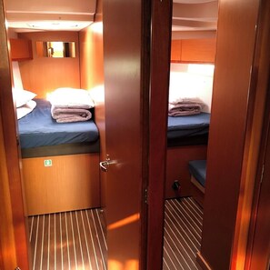 A narrow corridor with two beds, each with a blue mattress and pillows, and a small mirror on the wall. - Sun-Kissed Sailing Adventure in Islas Sarónicas (Alimos)