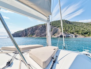 A boat's deck with seating, a view of the sea, and a mountainous coastline.