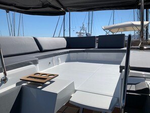 A boat's deck with seating, a wooden tray, and a clear view of the water and other boats. - Sun-Kissed Sailing Adventure in the Saronic Islands (Laurium)