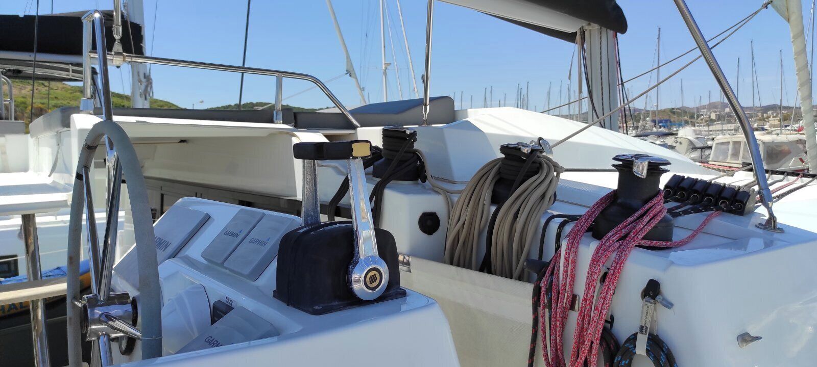 A boat's deck with a steering wheel, control panel, and coiled ropes.