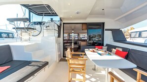 A yacht interior with a dining area, seating, and a view of the marina. - Sun-Kissed Sailing Adventure in the Stunning Islas Cícladas (Paros)