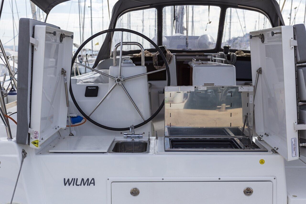 Interior de un barco con timón, un lavabo y el nombre de marca 'WILMA' en la cubierta.