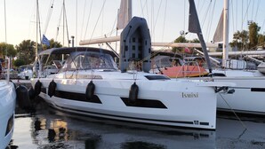 Een witte jacht genaamd 'Ismini' afgemeerd in een jachthaven, samen met andere boten, met een kajuit, reddingsboten en een mast.