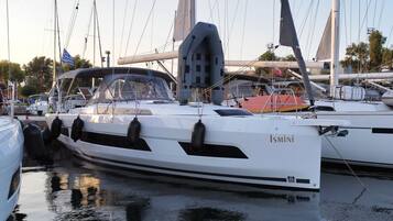 Un yacht blanc baptisé « Ismini » était amarré dans une marina, aux côtés d’autres bateaux. Il était équipé d’une cabine, de canots de sauvetage et d’un mât.