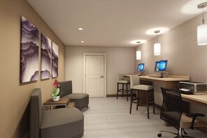 A hotel room with a desk, two chairs, a sofa, a TV, and artwork on the wall.
