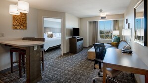 Quarto de hotel com cama, escrivaninha, cadeira, televisão e janela com vista.