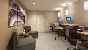 Hotellihuone, jossa on työpöytä, kaksi tuolia, sohva, televisio ja taideteoksia seinällä.
