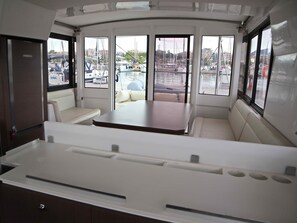 Schiffsinnenraum mit Sitzgelegenheiten, einem Tisch und Fenstern mit Blick auf eine Marina.