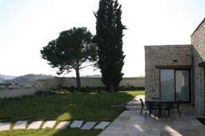 A patio with stone flooring, a table with chairs, and a tall tree. - Maison Lagerstroemie -Exclusive Villa with Private Pool in Le Marche, Filottrano (Filottrano)