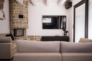 A modern living room with a stone fireplace, a flat-screen TV mounted on the wall, and a sofa. - Maison Lagerstroemie -Exclusive Villa with Private Pool in Le Marche, Filottrano (Filottrano)