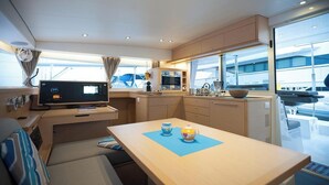 A compact kitchen with a TV, a dining table with two teapots, and a window overlooking the deck. - Sun-Kissed Sailing: A Luxurious Beach Experience in Nikiti, Macedonia (Nikiti)