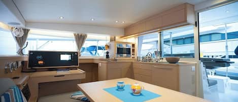 A compact kitchen with a TV, a dining table with two teapots, and a window overlooking the deck.