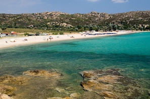 Une plage à l’eau turquoise et limpide, bordée de rivages rocheux et dominée par des collines.