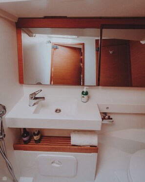Un baño con un lavamanos blanco, un espejo encima, una puerta de madera y un perchero para toallas.