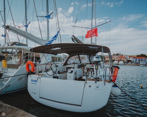 Un velero atracado en una marina, con cielo despejado, un flotador y una bandera.