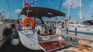 Ein Boot namens 'ELENI' liegt in einer Marina mit anderen Booten, einem Rettungsring und einer Flagge vor Anker.
