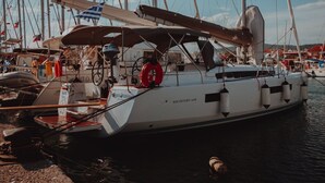 Eine Segelyacht liegt im Hafen festgemacht, zusammen mit mehreren anderen Booten, einem Rettungsring und einer Flagge.