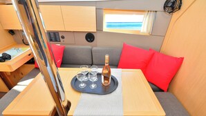 En kompakt opholdsstue med et bord dækket til et måltid, en flaske og glas, et lille vindue med udsigt og et kontrolpanel.