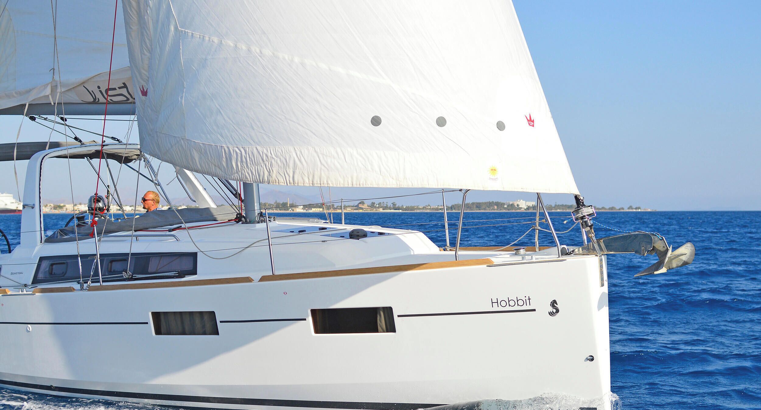 A sailboat named 'Hobbit' with a white hull, a cabin with windows, and a person wearing an orange life jacket.