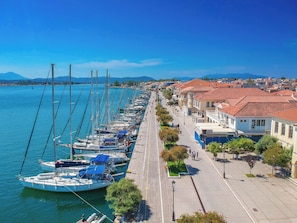 Ein Yachthafen mit vertäuten Booten entlang einer Uferpromenade, gesäumt von Gebäuden und Bäumen.