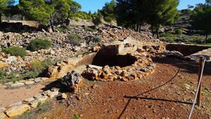 Sítio arqueológico rochoso com estruturas de pedra e árvores.