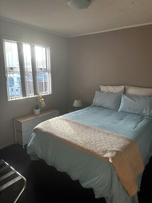 Ein Schlafzimmer mit Bett, Nachttischen, einem Fenster und einer Heizung.