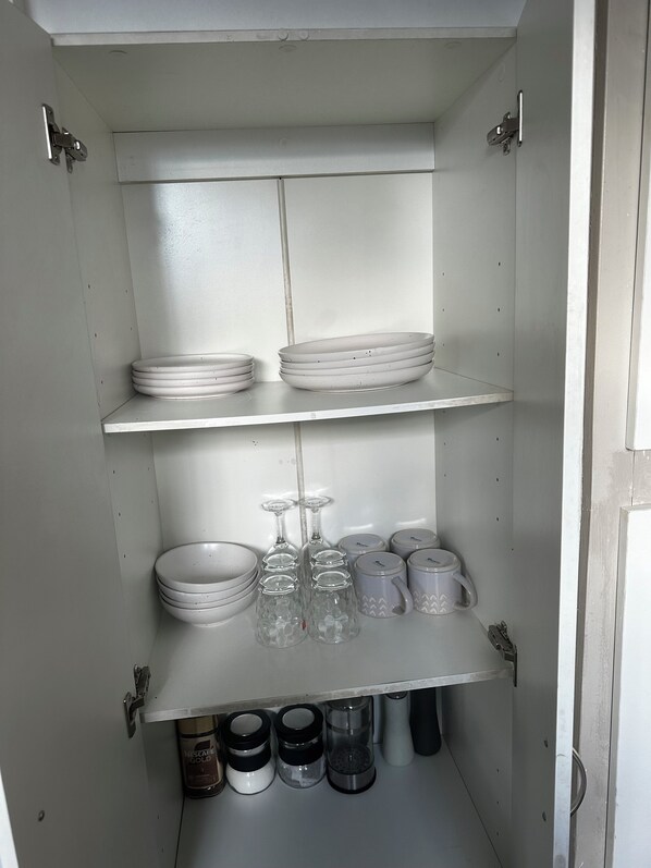 Un mueble de cocina con estantes que contienen platos, vasos y frascos.