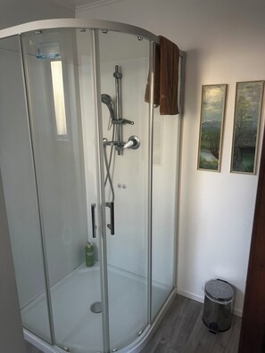 Ducha con cerramiento de vidrio, cabezal de ducha de mano y grifo empotrado.