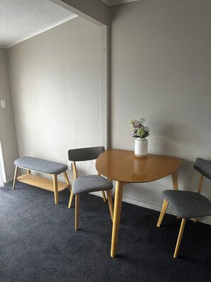 Una habitación con una mesa redonda de madera, cuatro sillas tapizadas de color gris, un pequeño florero blanco y una alfombra gris.