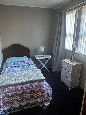 A hotel room with a bed, a bedside table with a lamp, a small cabinet, and a window with curtains. - GREY STREET HAVEN!
Relax and unwind in this peaceful home, (Rotorua)