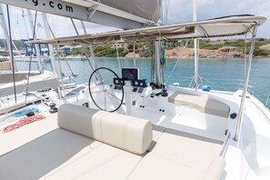 A boat deck with a steering wheel, control panel, and seating area. - Sun-Kissed Sailing Adventure in the Saronic Islands (Laurium)