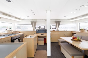 A modern kitchen with a stove, sink, and dining area with a table and benches. - Sun-Kissed Sailing Adventure in the Saronic Islands (Laurium)
