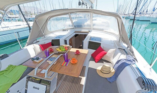 A boat interior with a dining table, cushions, a hat, and a B&G cooler. - Sun-Kissed Sailing Adventure in the Dodecanese Islands (Kos)