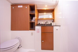 A compact bathroom with a toilet, wooden cabinets, a mirror, and a small sink area. - Sun-Kissed Sailing Adventure in Islas Sarónicas (Alimos)