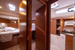 A compact RV interior with a bed, kitchenette, and a small bathroom. - Sun-Kissed Sailing Adventure in Islas Sarónicas (Alimos)