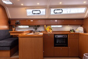 A compact kitchen with wooden cabinets, a built-in oven, and a small countertop. - Sun-Kissed Sailing Adventure in Islas Sarónicas (Alimos)