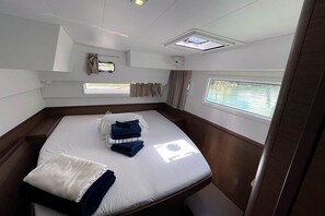 Une cabine comprenant un lit, une fenêtre, un puits de lumière et une petite fenêtre avec des rideaux.
